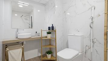 A modern bathroom with a white sink, mirror, toilet, and shower.