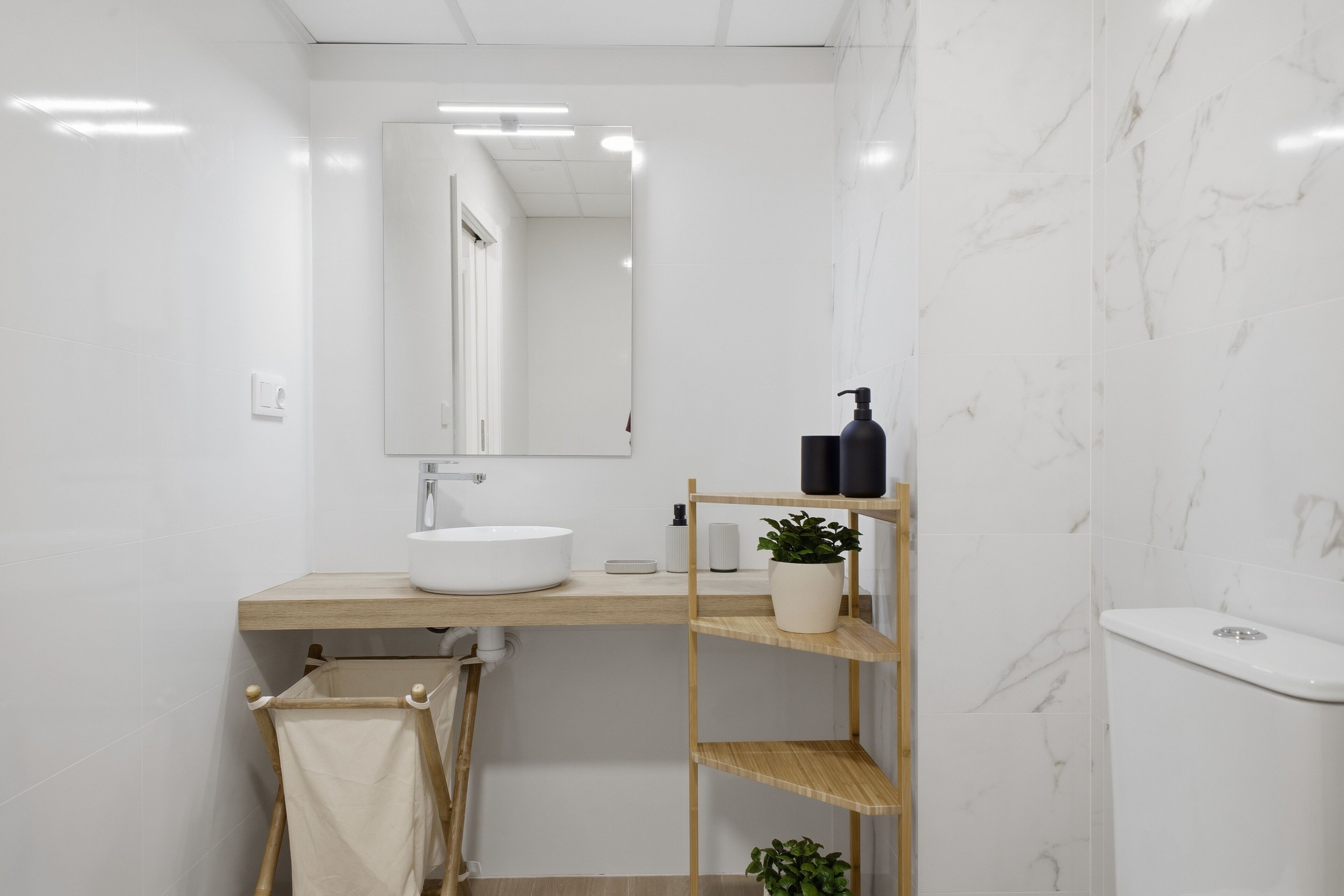 A modern bathroom with a white sink, mirror, and marble walls.