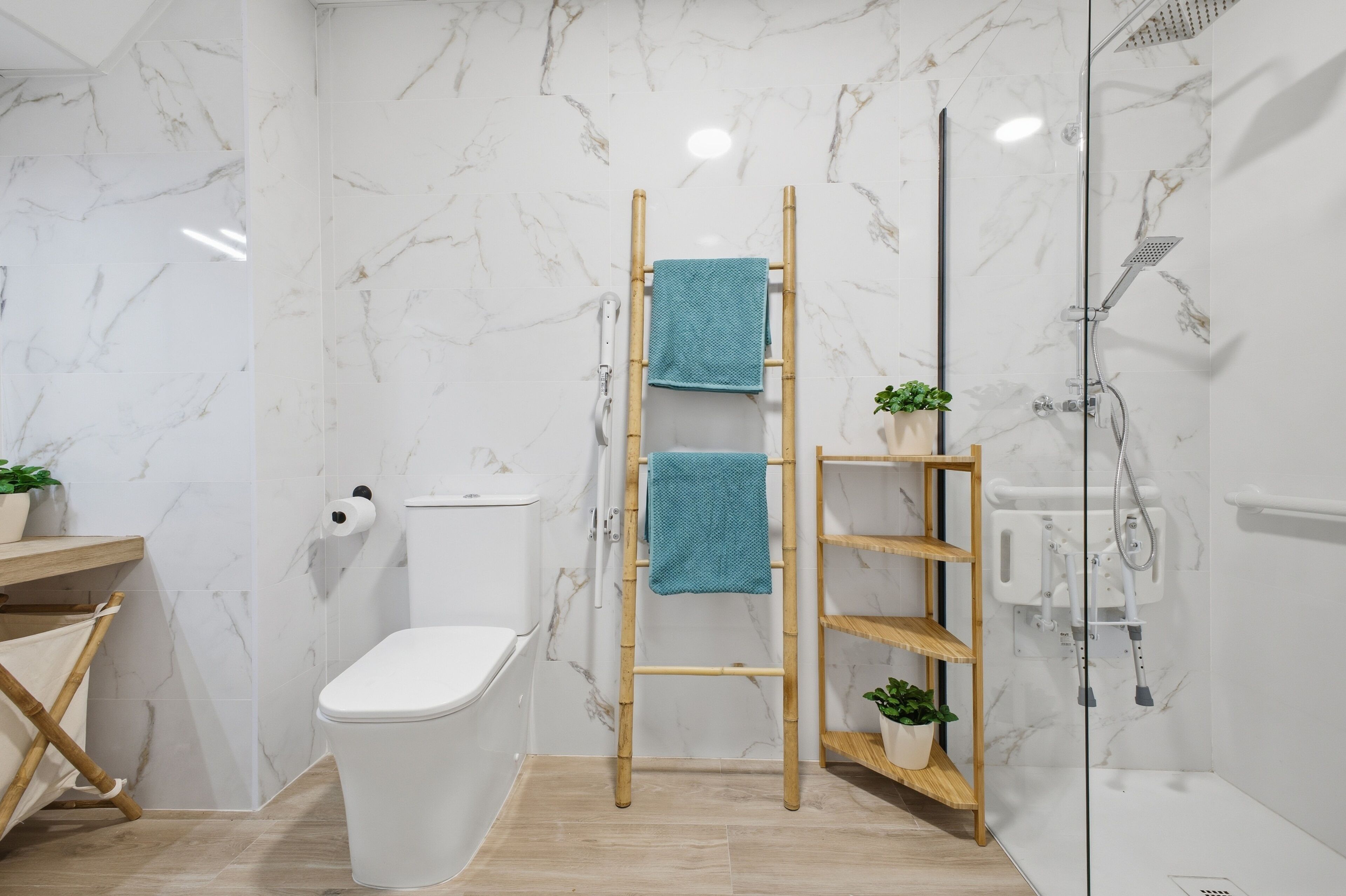 Un baño con inodoro, ducha con puerta de cristal, escalera de madera y dos estantes con plantas.