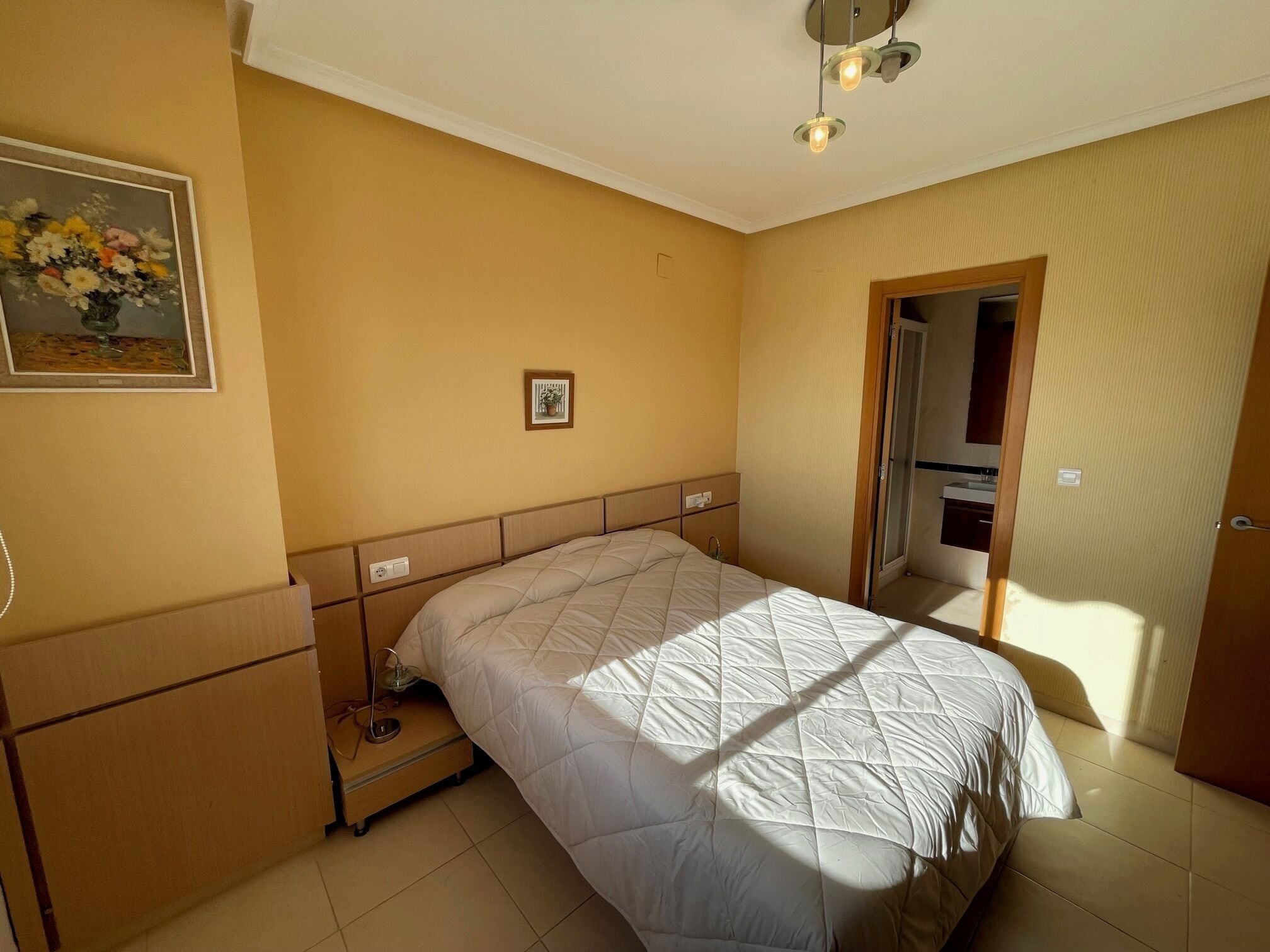 Un dormitorio con cama, mesita de noche y lámpara fijada a la pared.