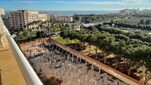 A high-rise building with balconies overlooking a coastal cityscape, palm trees, and a park with a sculpture. - Spacious 2-bedroom Apartment With Pool View in Oropesa del Mar (Oropesa del Mar)