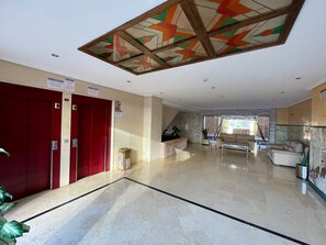 Un hall d’hôtel avec un ascenseur rouge, un escalier en verre et un espace salon offrant une vue sur l’extérieur.