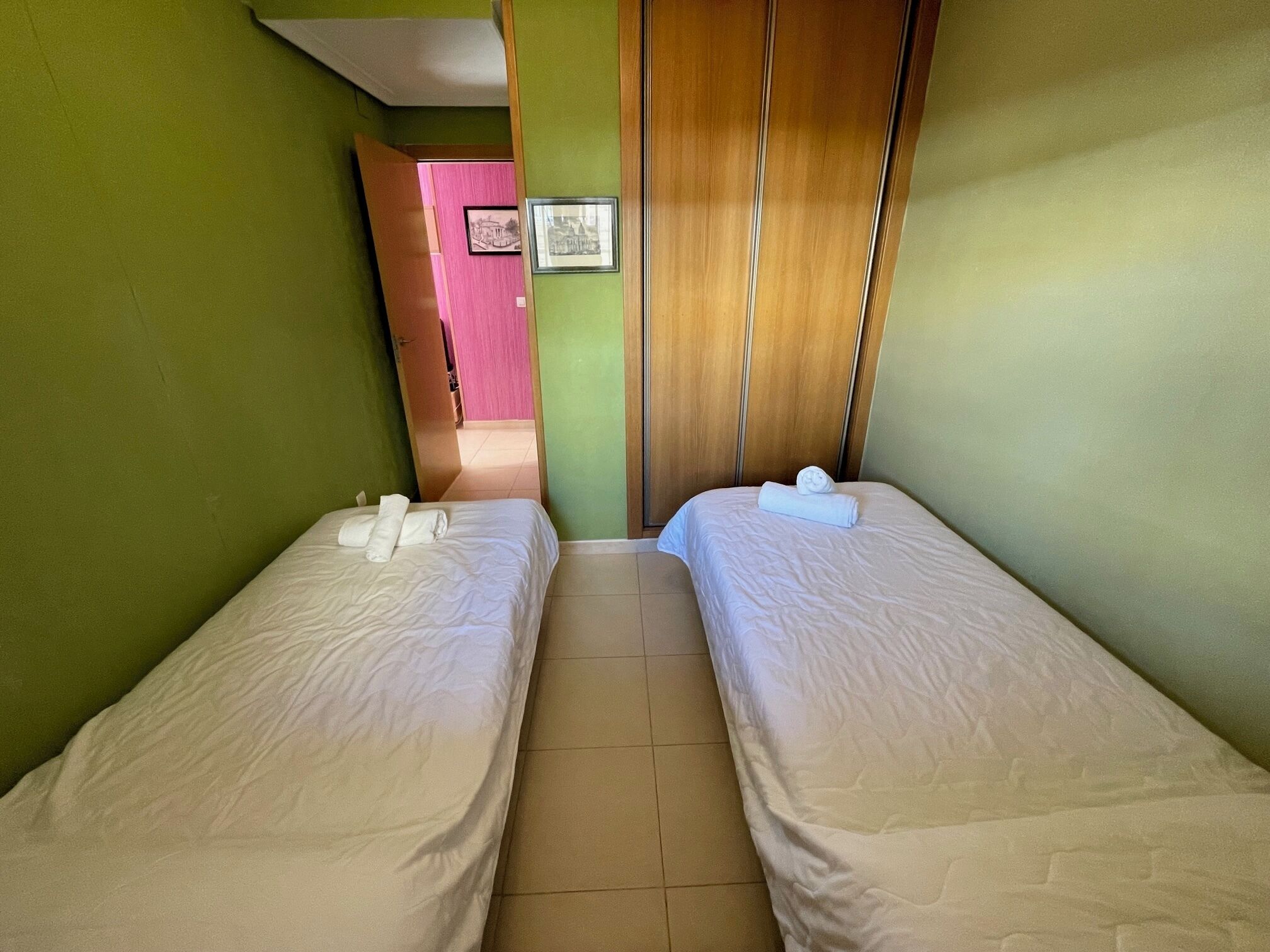 A room with two beds, a wooden wardrobe, and a door leading to another room.