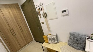 A room with a wooden wardrobe, a small table with a cushion, a thermostat, and a fluffy pillow. - Cozy house in nouvelle soukra (Ariana)