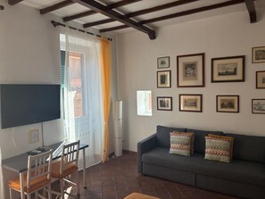 A living room with a TV, dining table, chairs, a sofa with patterned cushions, and framed pictures on the wall. - The Yellow Nest Apartment in Trastevere (Roma)