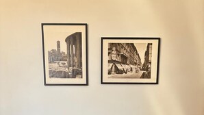 A dining table with two chairs, a set of four mugs, a small clock, and two framed pictures on the wall. - The Yellow Nest Apartment in Trastevere (Roma)
