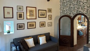 A room with a grey sofa, multiple framed pictures on the wall, a mirror, and a patterned wallpaper. - The Yellow Nest Apartment in Trastevere (Roma)