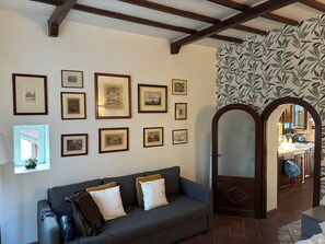 A room with a grey sofa, multiple framed pictures on the wall, a mirror, and a patterned wallpaper. - The Yellow Nest Apartment in Trastevere (Roma)