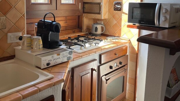 A compact kitchen with a gas stove, a kettle, a microwave, and wooden cabinets. - The Yellow Nest Apartment in Trastevere (Roma)