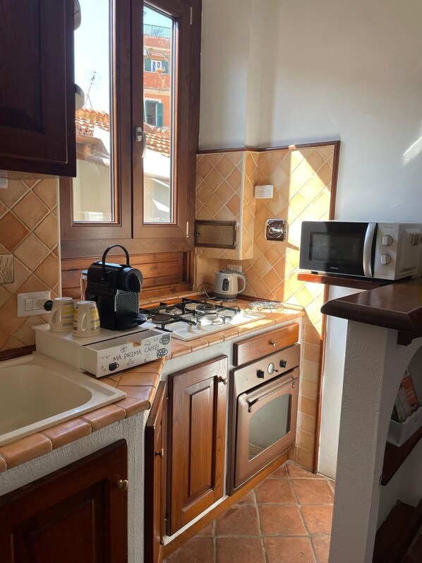A compact kitchen with a gas stove, a kettle, a microwave, and wooden cabinets. - The Yellow Nest Apartment in Trastevere (Roma)