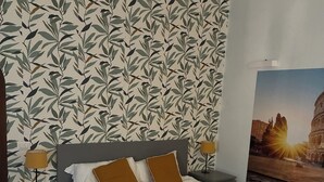 A bedroom with a bed, nightstands, a lamp, a patterned wallpaper, and a large poster of a building. - The Yellow Nest Apartment in Trastevere (Roma)