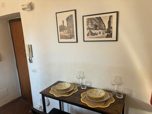 A dining area with two framed black and white photographs on the wall, a wooden table with two plates and cutlery, and two wine glasses. - The Yellow Nest Apartment in Trastevere (Roma)