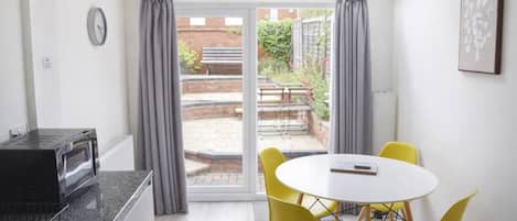 A modern kitchen with a built-in microwave, a dining area with a round table and yellow chairs, and a sliding glass door leading to an outdoor patio.