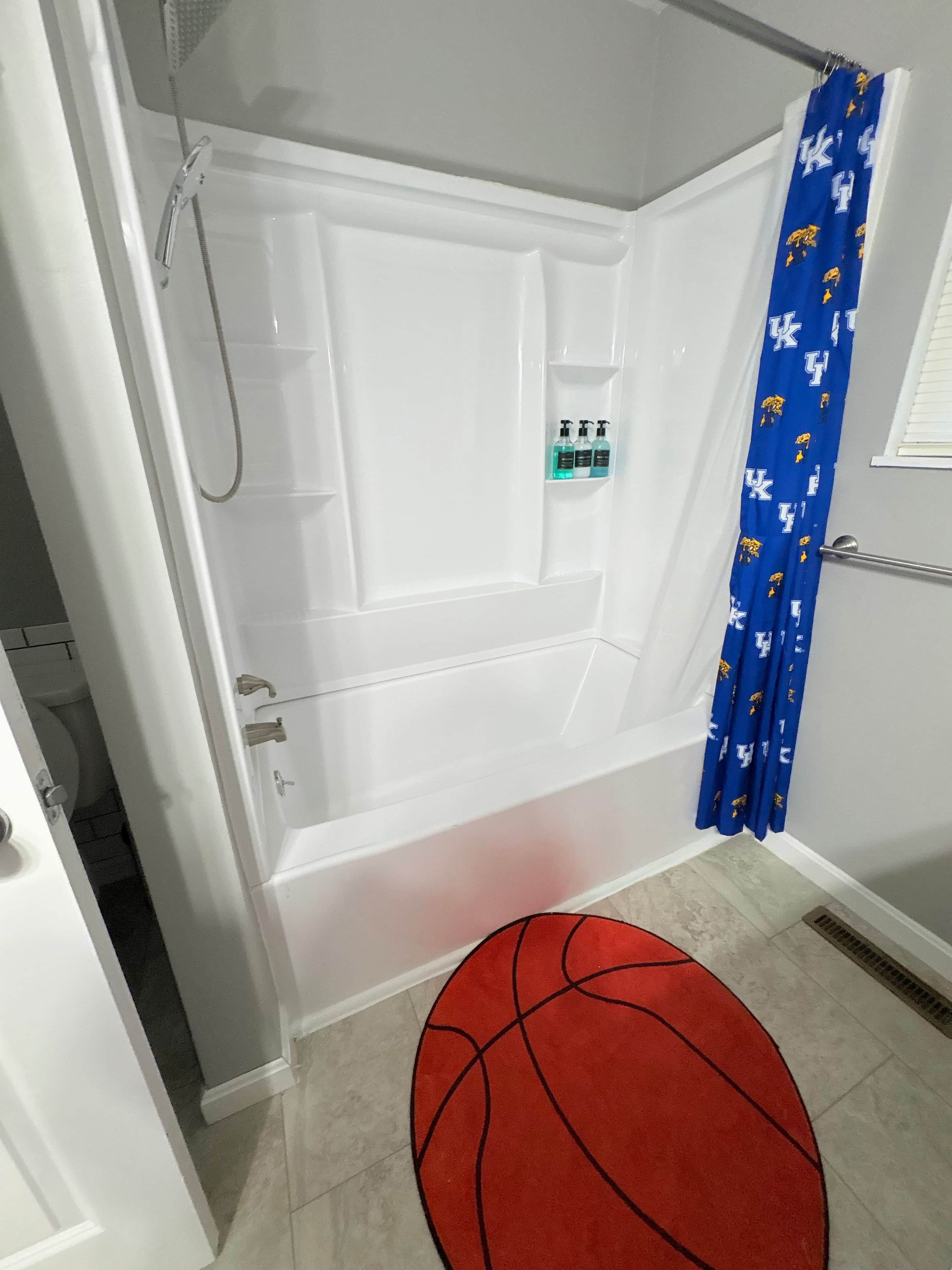 Un baño con bañera, cortina de ducha y una alfombra con motivos de baloncesto.