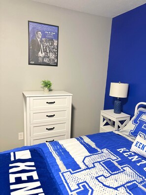 A bedroom with a bed featuring blue and white bedding, a dresser, a nightstand with a lamp, and a poster on the wall. - The Swish & Stay I Cozy 2BR I 15m to RRG I Wi-Fi (Stanton)
