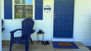 Une porte d’entrée avec une pancarte, une chaise bleue, une petite table et un paillasson.