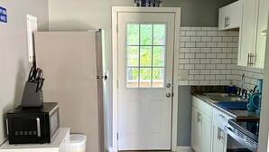 Une cuisine compacte avec un réfrigérateur blanc, un four à micro-ondes et un four traditionnel. Une porte avec une fenêtre et une enseigne au-dessus.