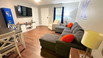 Een woonkamer met een bank, een eettafel, stoelen, een televisie en een lamp.