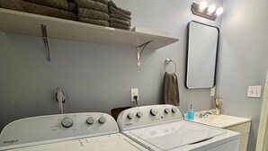 Une buanderie équipée de deux machines à laver et de deux sèche-linge Whirlpool, d’un évier et d’un porte-serviettes.