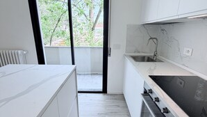 Una cucina moderna con mobili bianchi, un piano cottura nero e una finestra che si affaccia su alberi.