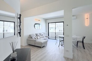 Een moderne woonkamer met een bank, een eettafel met stoelen en een groot raam.