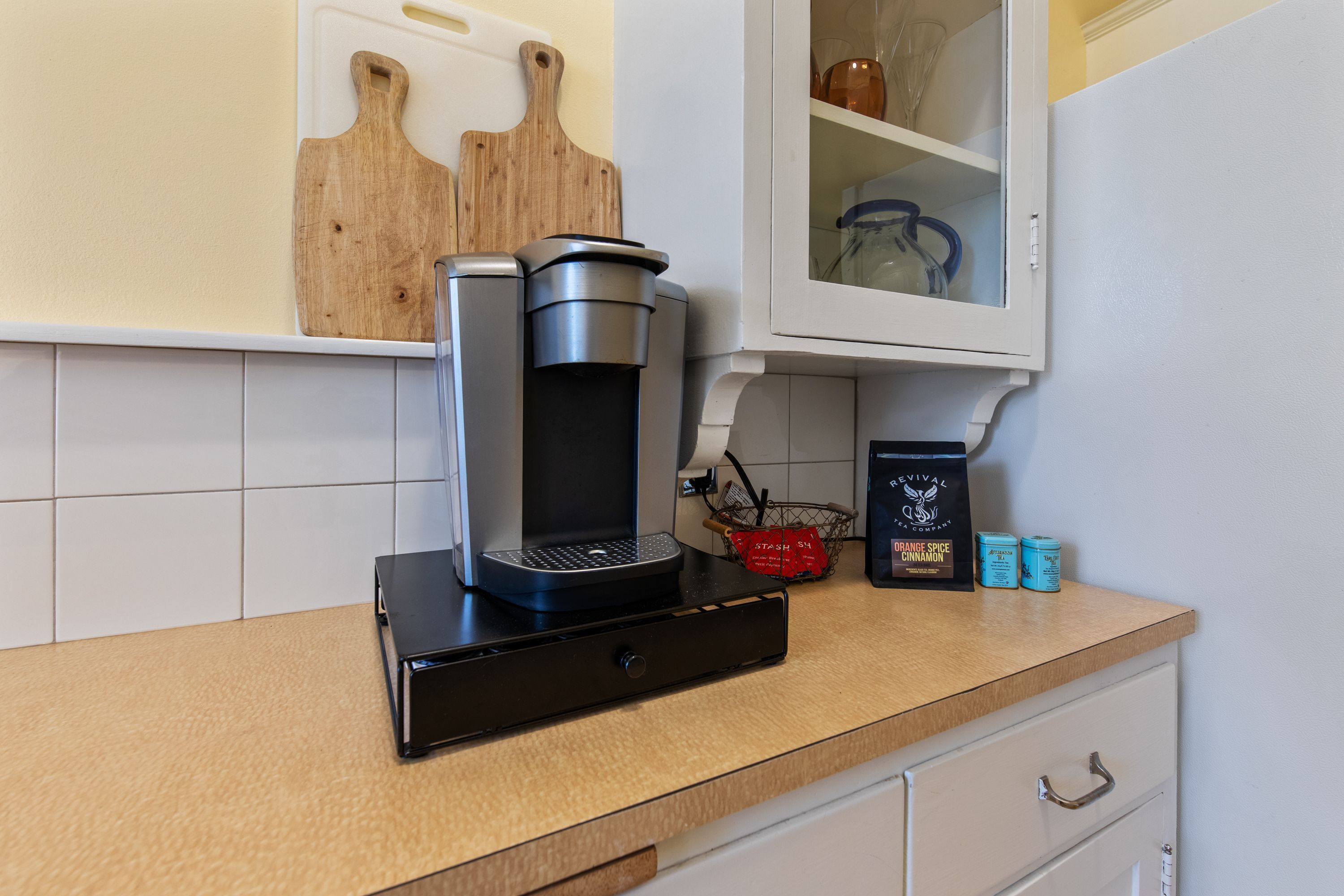 Una cucina con una macchina da caffè, un tagliere, una spezieria e un armadietto.
