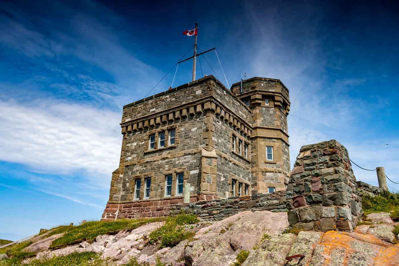 A stone building with a flag, windows, and a tower.