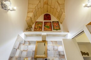Ein Badezimmer mit Bogen aus Stein, einem Spiegel und religiösen Bildern an der Wand.