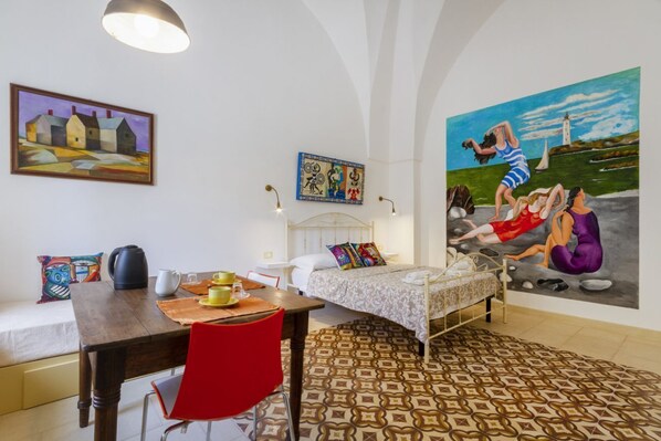 Ein Zimmer mit einem Bett, einem Esstisch, einem roten Sessel, einem Bild an der Wand und einem gemusterten Teppich.