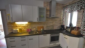 A compact kitchen with white cabinets, a built-in oven, and a stone backsplash. - Apartment V+K – Cozy 2BR near High Tatras, Štrba (Štrba)