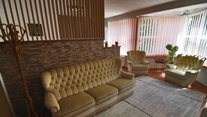 A living room with a sofa, armchairs, a wooden floor, a stone wall, and a window with blinds. - Apartment V+K – Cozy 2BR near High Tatras, Štrba (Štrba)