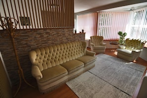 Una sala de estar con sofá, sillones, suelo de madera, pared de piedra y una ventana con persianas.