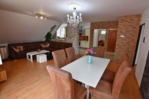 Ein modernes Wohnzimmer mit Essbereich, einer Chandelüster und einer Küche im Hintergrund.