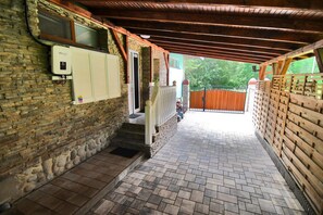 Un espace extérieur abrité, doté d’un mur en briques, d’une porte en bois et d’un chemin pavé.