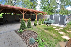 Un porche cubierto con un banco de madera y un pequeño jardín con diversas plantas.