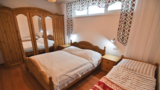 A bedroom with two single beds, a wooden wardrobe, a bedside table with a lamp, and a window with floral curtains. - Apartment V+K – Cozy 2BR near High Tatras, Štrba (Štrba)