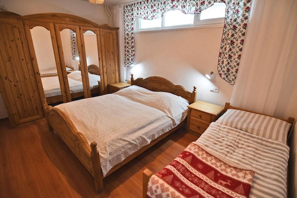 Un dormitorio con dos camas individuales, un armario de madera, una mesita de noche con lámpara y una ventana con cortinas florales.