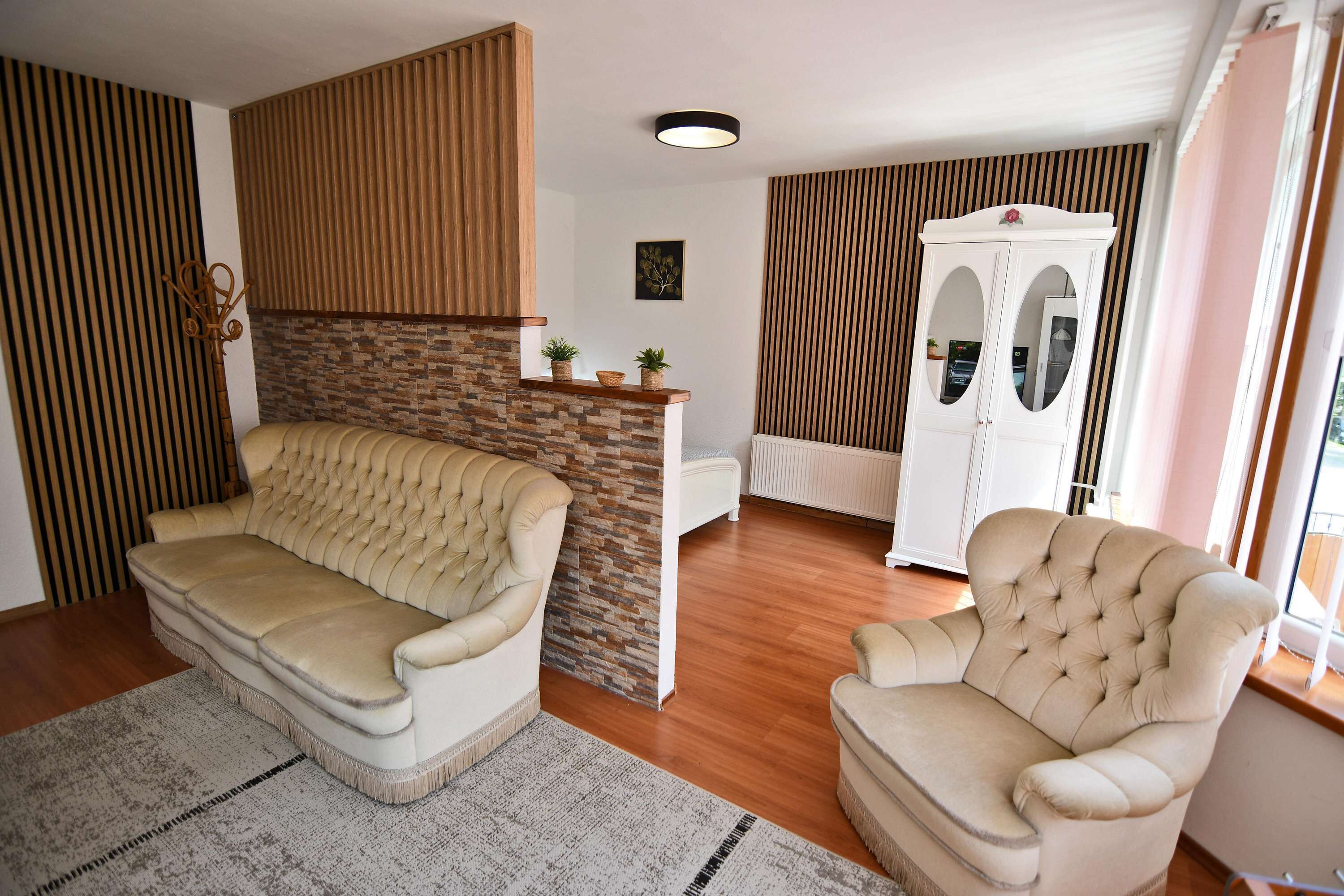 A living room with a beige sofa, a white armchair, a stone accent wall, and a wooden panel wall.