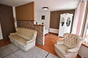 Un saló amb un sofà beix, un butàc armchair blanc, una paret decorativa de pedra i una paret revestida de fusta.