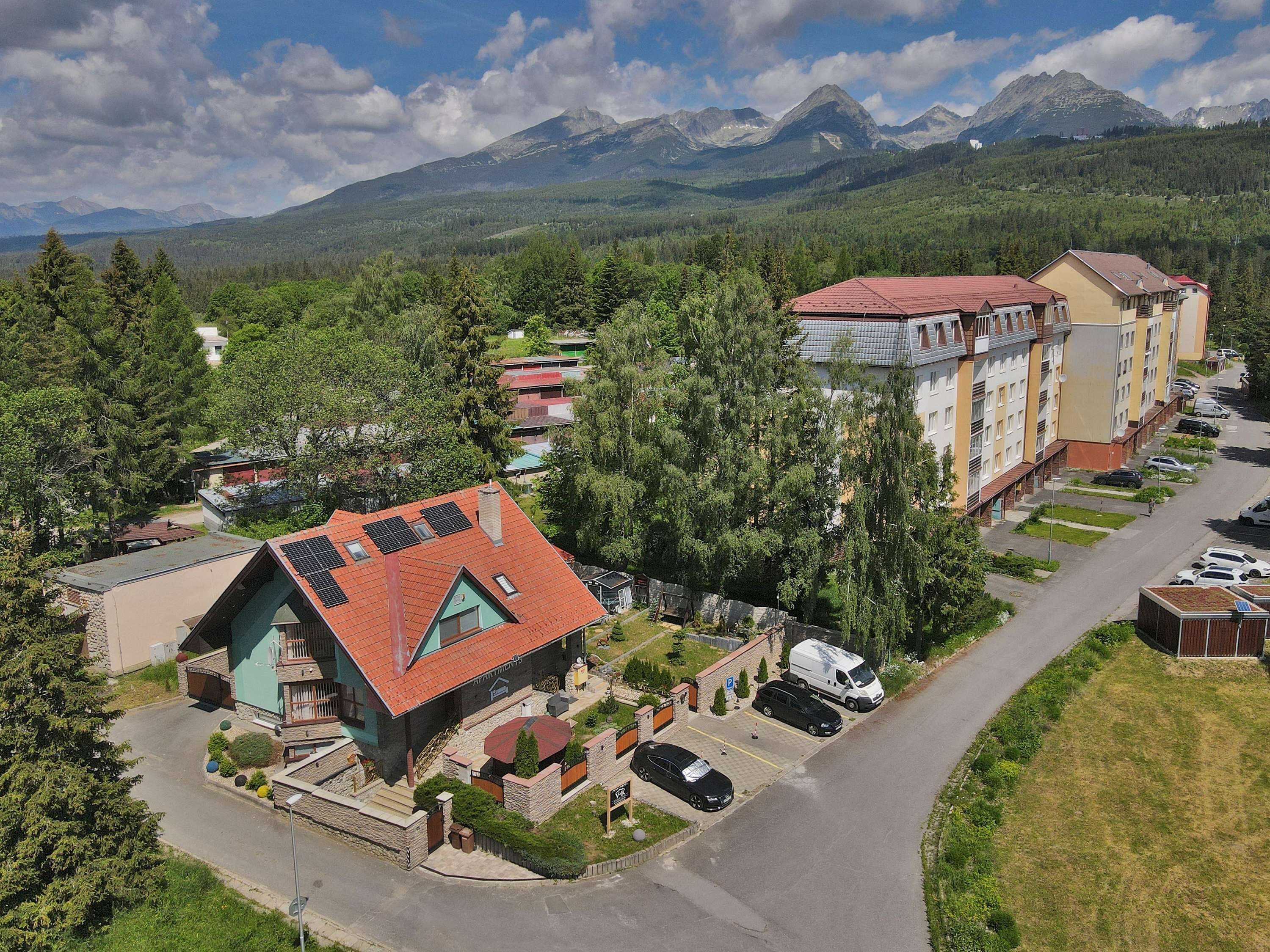 A residential area with a mix of single and multi-story buildings, a parking area, and a road leading to a mountain range.
