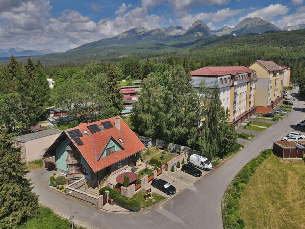A residential area with a mix of single and multi-story buildings, a parking area, and a road leading to a mountain range.