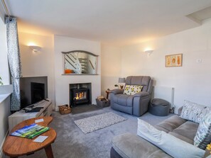 Ein Wohnzimmer mit Kamin, einer Couch, einem Sessel, einem Fernseher und einem Couchtisch.