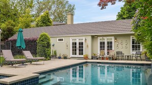 Une piscine avec des chaises longues, un patio couvert et une maison avec un toit en tuiles et un mur décoratif.