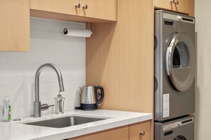 A kitchen with a stainless steel sink, a kettle, and a built-in washing machine. - Modern Studio | Pool + Hot Tub, Land Park Area (Sacramento)