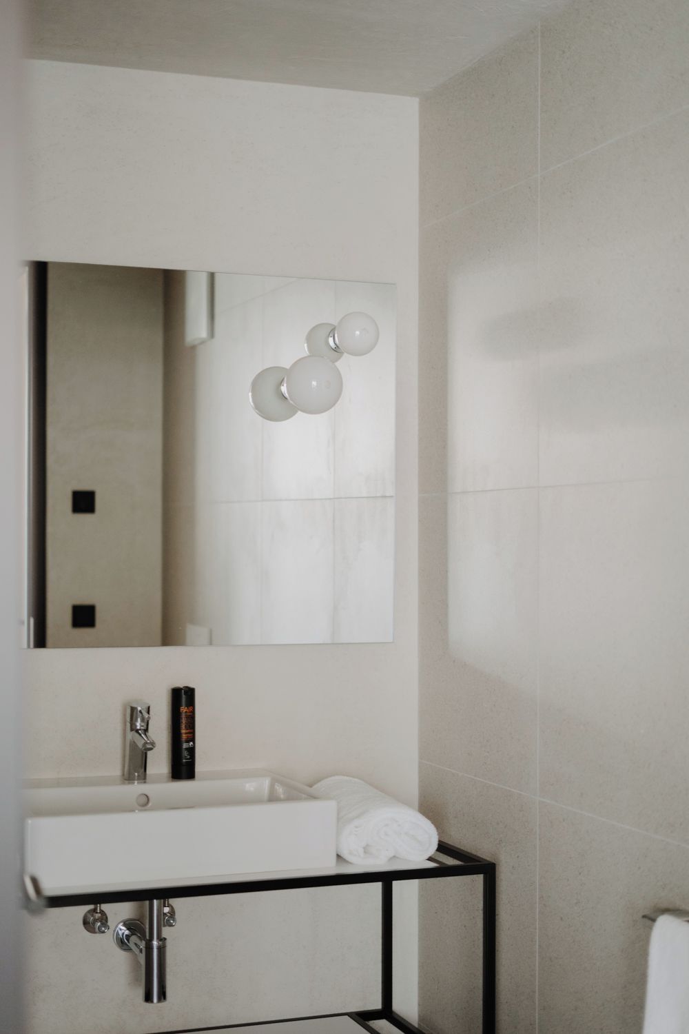 Un baño moderno con un lavamanos blanco, un soporte de metal negro, un espejo y un perchero.