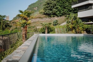 Une piscine avec vue sur un château en arrière-plan, entourée de verdure et bordée d’un bâtiment moderne.