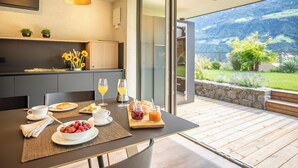 A dining area with a table set for breakfast, a kitchen in the background, and a view of a mountainous landscape through a glass door. - Marchegg Apartments (Naturno)