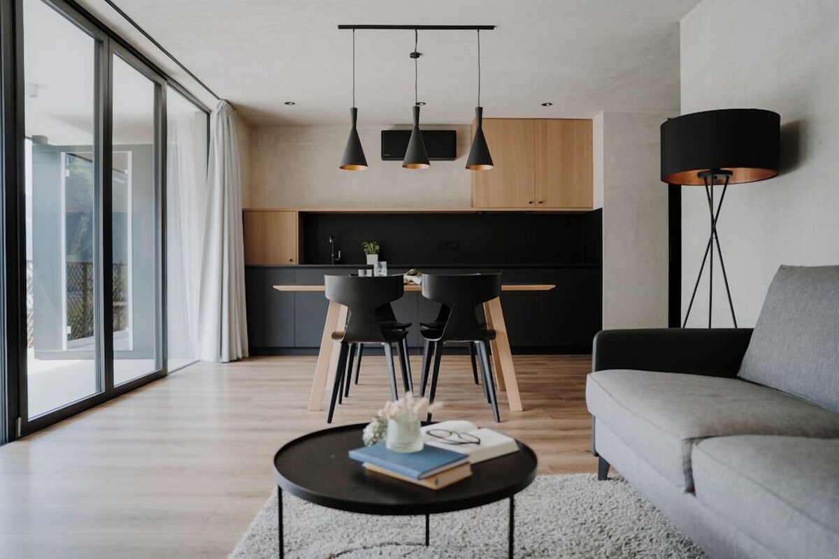 A modern living room with a sofa, a coffee table, and a dining area with chairs and a TV.