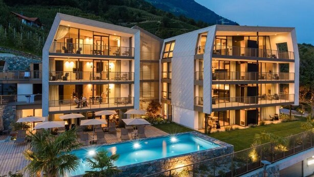 A modern hotel with multiple balconies, a swimming pool, and a mountainous backdrop. - Marchegg Apartments (Naturno)