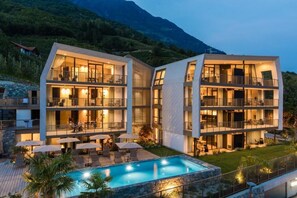 A modern hotel with multiple balconies, a swimming pool, and a mountainous backdrop. - Marchegg Apartments (Naturno)